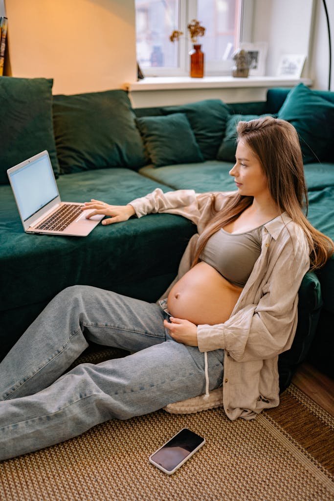 Pregnant woman sitting on floor with laptop, enjoying a calm day at home.